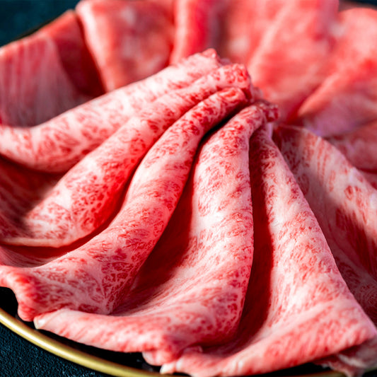 きめ細かな霜降りが全体に広がる佐賀牛の薄切りロースが、金縁の皿の上で花びらのように扇形に重なり、鮮やかな赤みと白い脂のコントラストを見せている