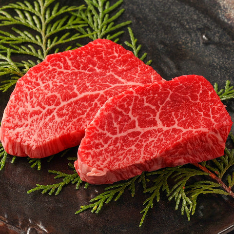 和牛モモステーキの生肉2枚を黒い陶器の器にヒバの葉を添えて盛り付け、鮮やかな赤身と細かく入った白い霜降りのコントラストが美しい