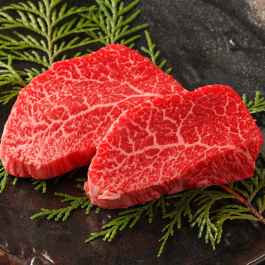 前沢牛モモステーキの生肉2枚を黒い陶器の器にヒバの葉を添えて盛り付け、鮮やかな赤身と細かく入った白い霜降りのコントラストが美しい