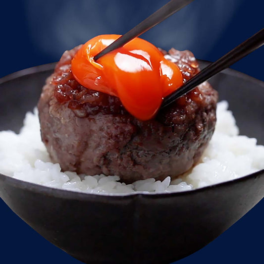黒い器に白ご飯とハンバーグを盛り付け湯気が立つなか橙色に輝く黄身を箸でつかんで垂らそうとしている食欲をそそる接写