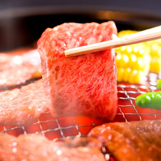 焼き網の上に並ぶ黒毛和牛の赤身肉を箸でつまみ上げた瞬間、鮮やかな赤色ときめ細やかな肉質が際立っている