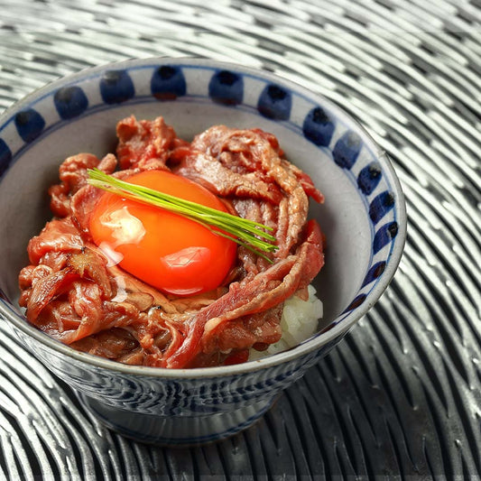 鳥取和牛の切り落としを使った牛丼が白と藍の和柄茶碗に盛られ、生卵と細ねぎを添えた仕上がり