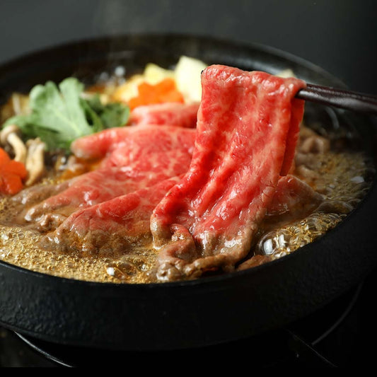 鳥取和牛のすき焼き肉を箸でつまみ上げた場面で、割り下が煮立つ鉄鍋の中に野菜と一緒に盛り付けられた料理の様子