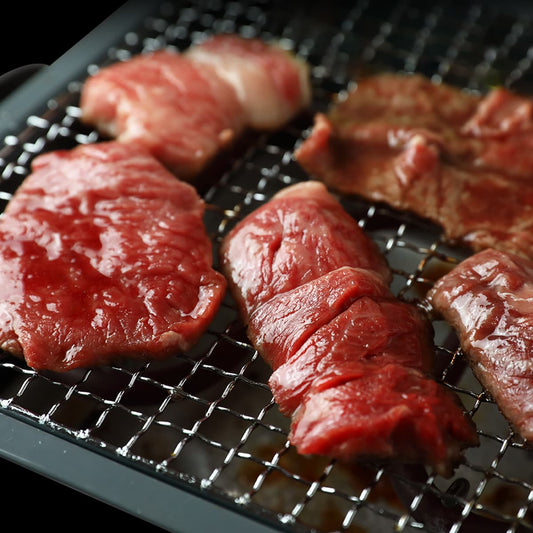 赤身肉の焼肉用カットが鉄製焼き網の上に並べられ、鮮やかな赤色とほどよい厚みが引き立つ焼き始め前の状態