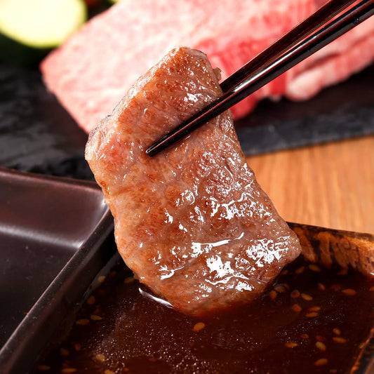 箸でつまみ上げた山形牛カルビの焼き上がり。照りのある褐色の表面からジューシーな脂がしたたり落ち、奥には生の霜降り肉が見える