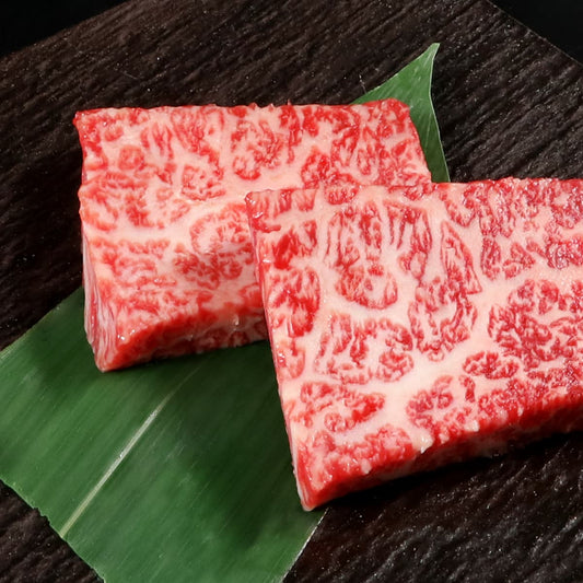 霜降りと赤身が美しく交差した松阪牛の厚切りステーキ用カット2枚が笹の葉の上にクローズアップで置かれている