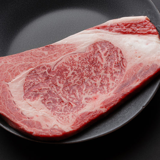 黒いフライパンに置かれたリブロースの大判生肉。全体にきめ細かなサシが入り、鮮やかな赤身とのコントラストが際立つ断面の美しさが伝わってくる