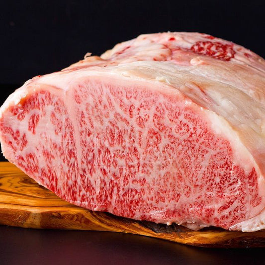 黒毛和牛のブロック肉をカッティングボードに置いた断面で、白とピンクの美しい霜降りが全面に広がっている