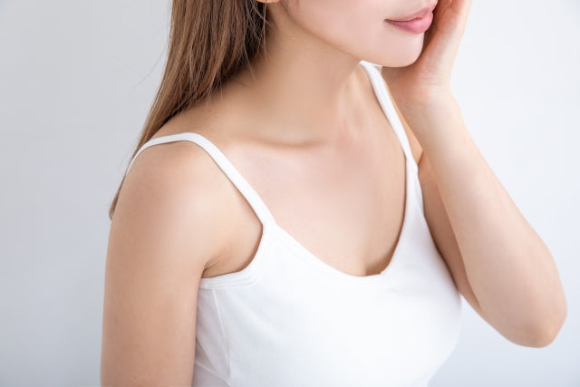 白いキャミソールを着た女性が頬に手を当てて横を向いており、首から肩にかけての滑らかな肌のラインと細い二の腕が際立っている