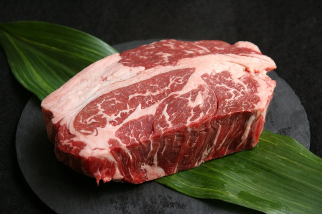 竹の葉を敷いた黒いスレートの上に置かれた和牛のブロック肉。全体に細かい霜降りが入り、鮮やかな赤色をしている