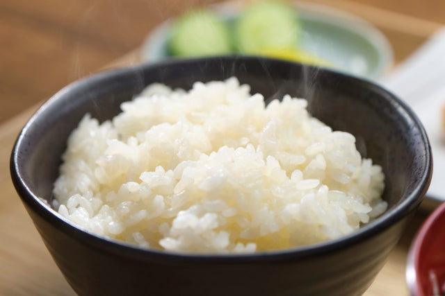 湯気の立ち上る炊きたての白いご飯が黒い茶碗に盛られており、お米ダイエットで活用できる主食の一例