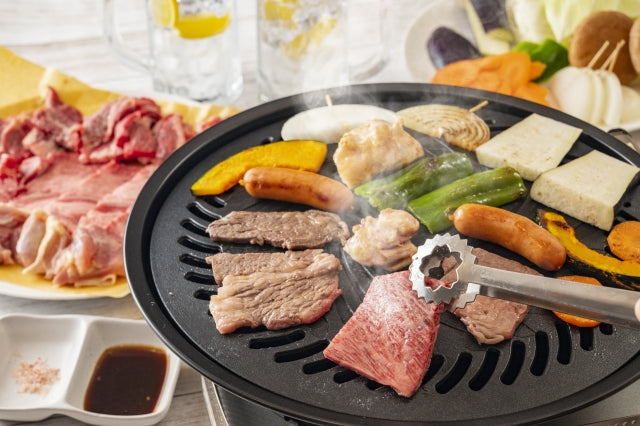 丸型ホットプレートの上で和牛や鶏肉、ウインナー、アスパラガスやかぼちゃなどの野菜を同時に焼いているホームパーティーの食卓
