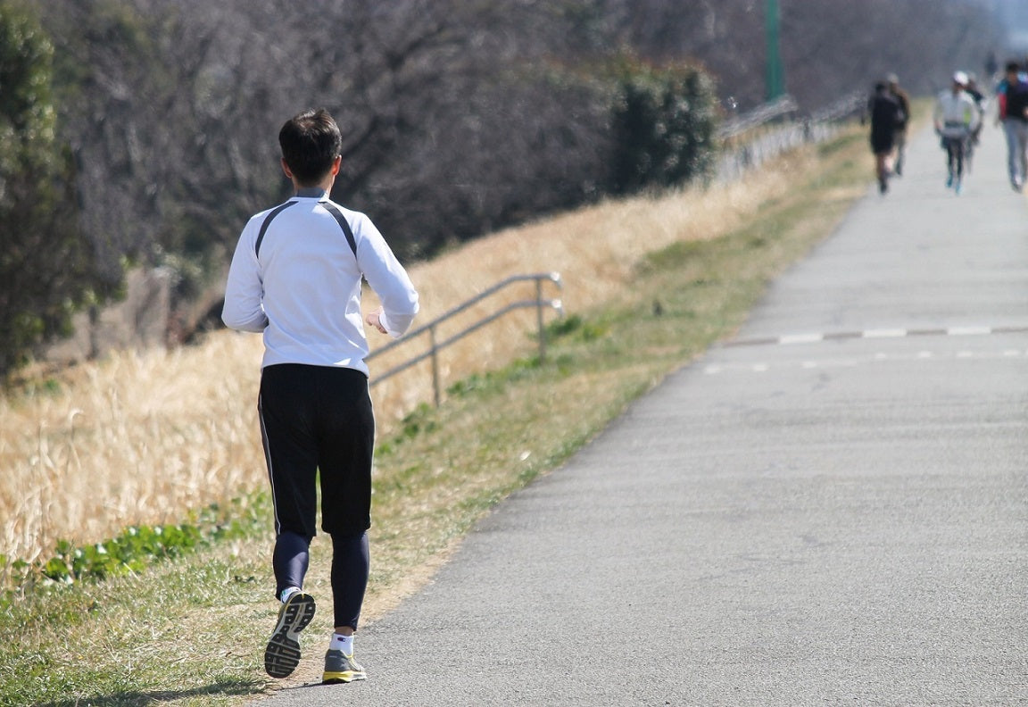 河川敷の舗装された遊歩道をランニングする男性の後ろ姿、有酸素運動による脂肪燃焼を目指すシーン