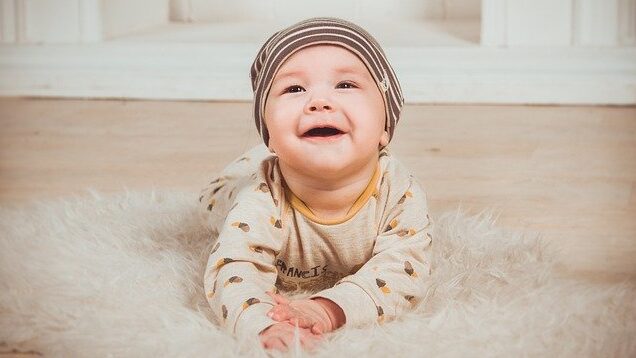 白いふわふわのラグの上でうつ伏せになり、満面の笑みを見せる帽子をかぶった赤ちゃん。子どものお祝いギフトにお肉を贈るコラムのアイキャッチ