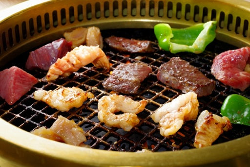 丸い焼き網の上で牛肉の各部位や海老などが一枚ずつ丁寧に焼かれており、赤身や脂身の焼き加減が食欲をそそる焼肉の様子