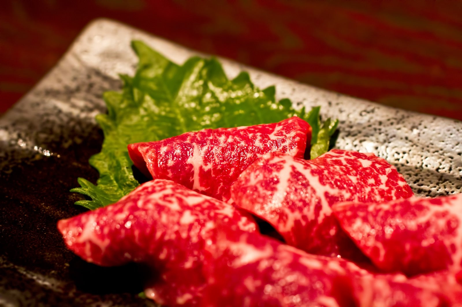 鮮やかな赤身に細かい霜降りが入った和牛の焼肉用スライスが、紫蘇の葉を添えた黒い皿に盛り付けられている