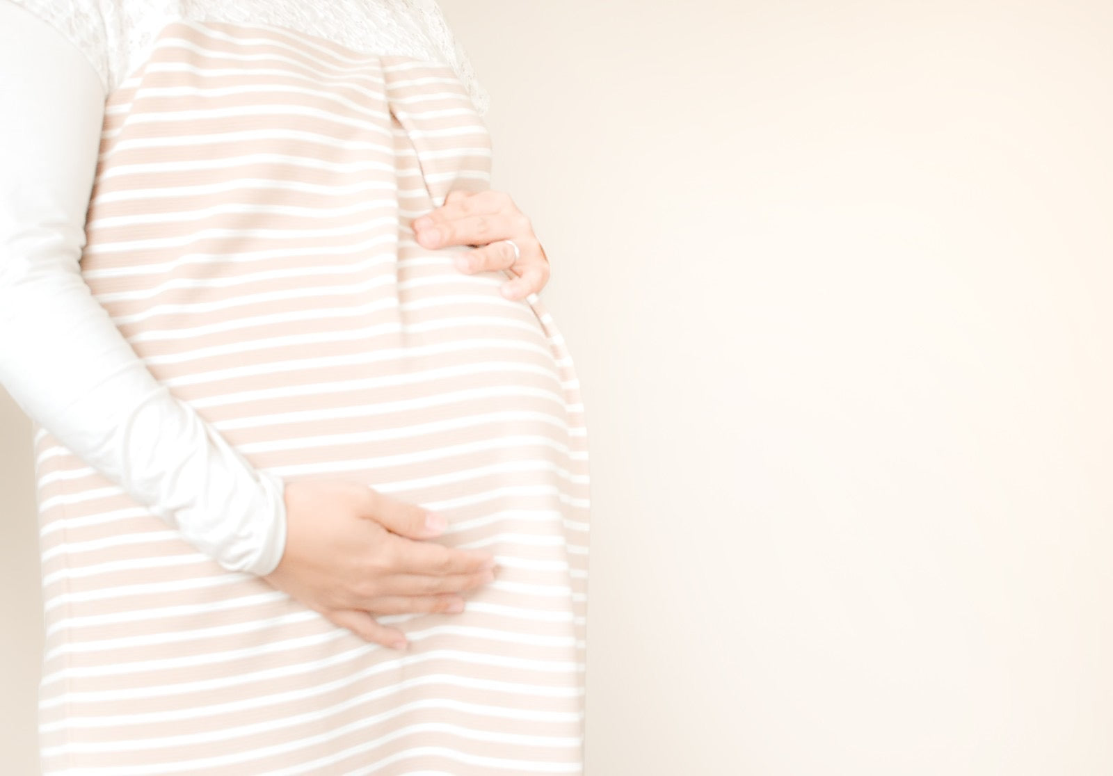 ボーダー柄の服を着た妊婦が両手でお腹を優しく支えており、産後の体型変化を意識した産後ダイエットのテーマを表している