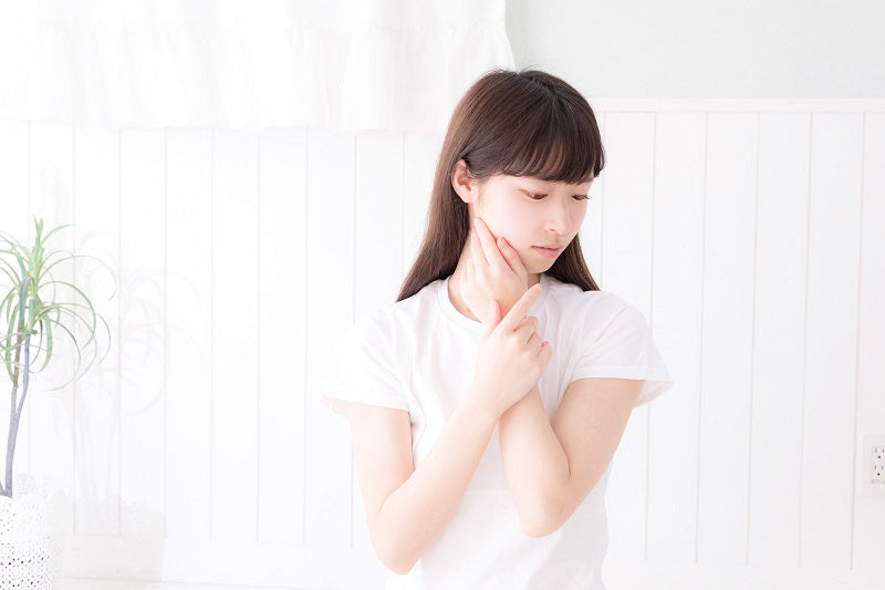 頬に手を当てて下を向く若い女性がアンチエイジングや肌の老化について考えている様子