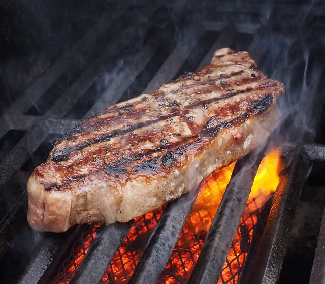 炭火グリルの上で焼き色がついた牛もも肉のステーキが炎を背に煙を上げている