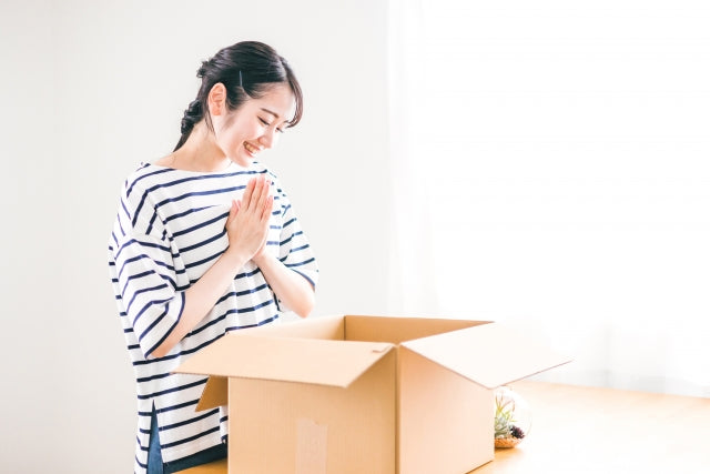 ボーダーTシャツを着た女性が笑顔で段ボール箱を覗き込み、両手を合わせて喜んでいる和牛ハンバーグお取り寄せの開封シーン