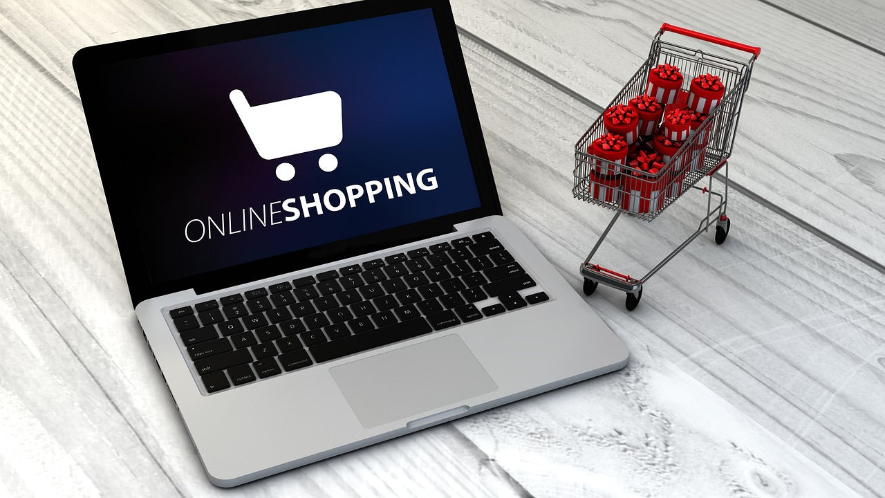 ONLINE SHOPPINGと表示されたノートパソコンの横に、赤いリボン付きギフトボックスを詰めたミニチュアのショッピングカートが置かれている