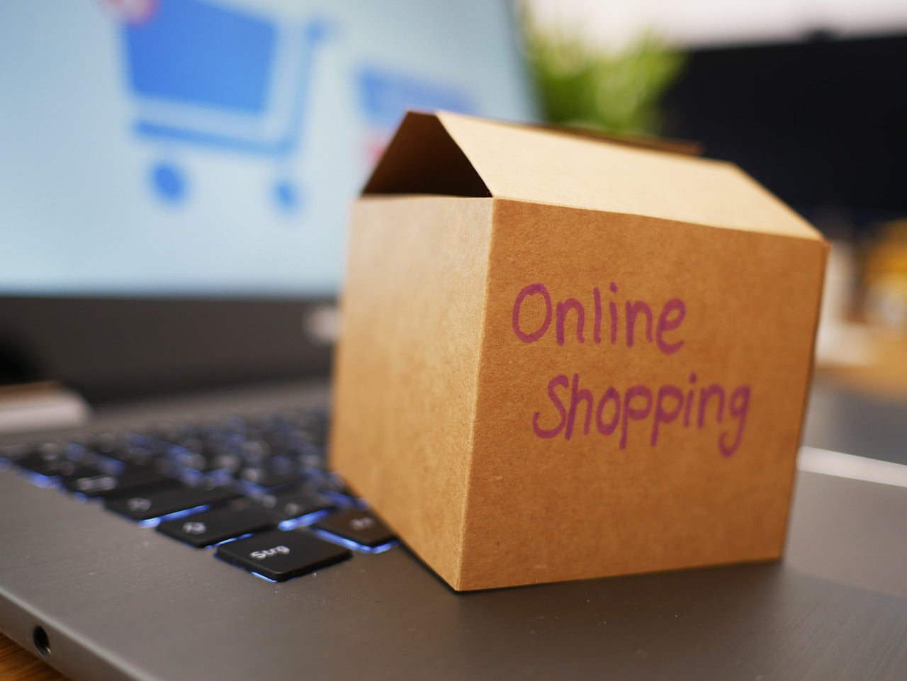 ノートパソコンのキーボードの上に置かれたクラフト紙の小箱にOnline Shoppingと書かれており、神戸牛ハンバーグを通販で選ぶ際のイメージを表している
