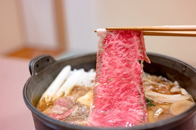 箸で持ち上げた霜降り和牛のすき焼き。甘辛い割り下が煮立つ鍋を囲む年末年始のご馳走