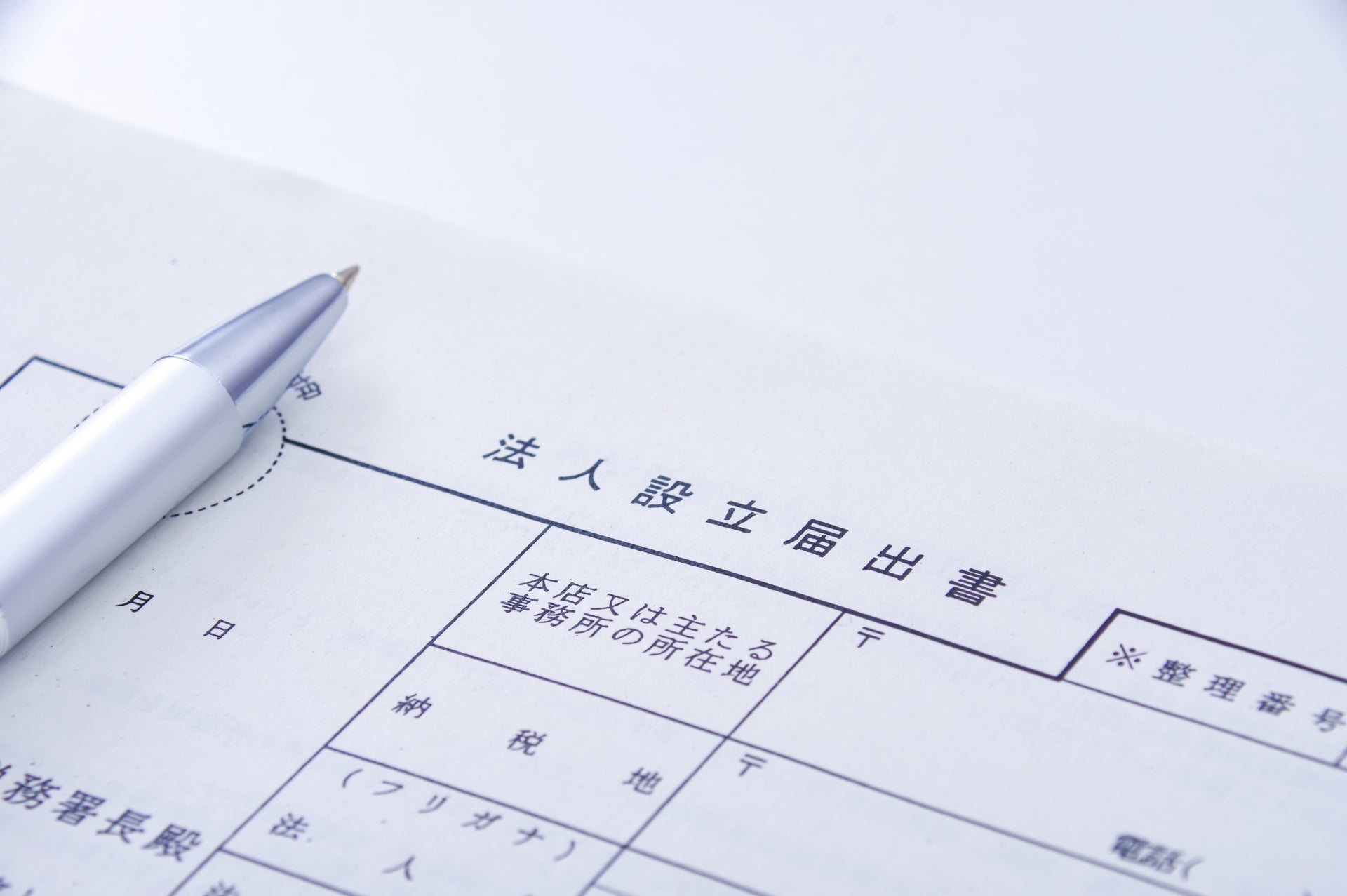 法人設立届出書と銀色のボールペンが白いデスクに置かれ、法人ギフトの贈り先となる取引先との関係を連想させる書類のクローズアップ