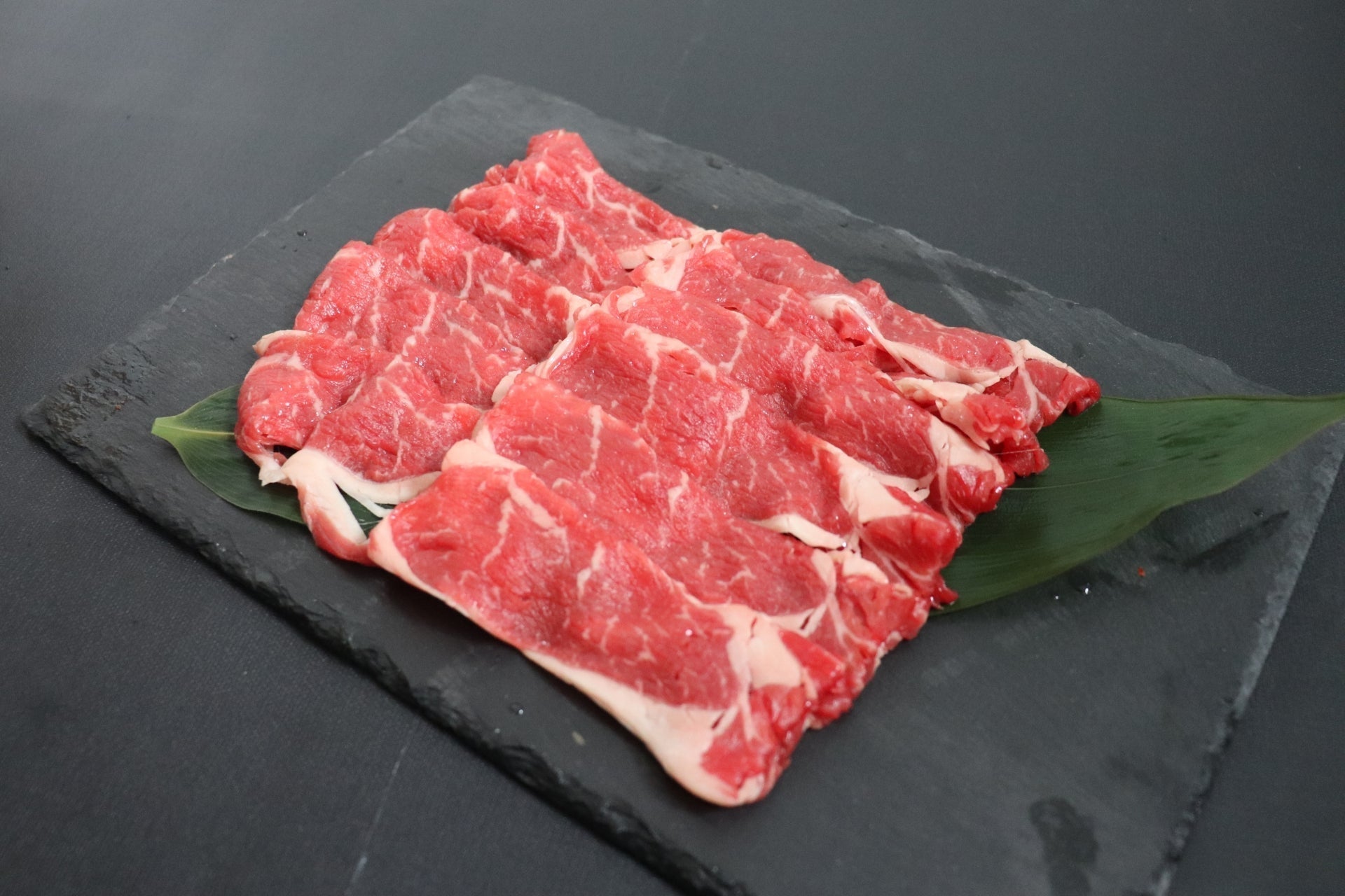 黒いスレートボードの上に笹の葉を敷き、薄切り牛肉を重ならないよう丁寧に並べた盛り付け