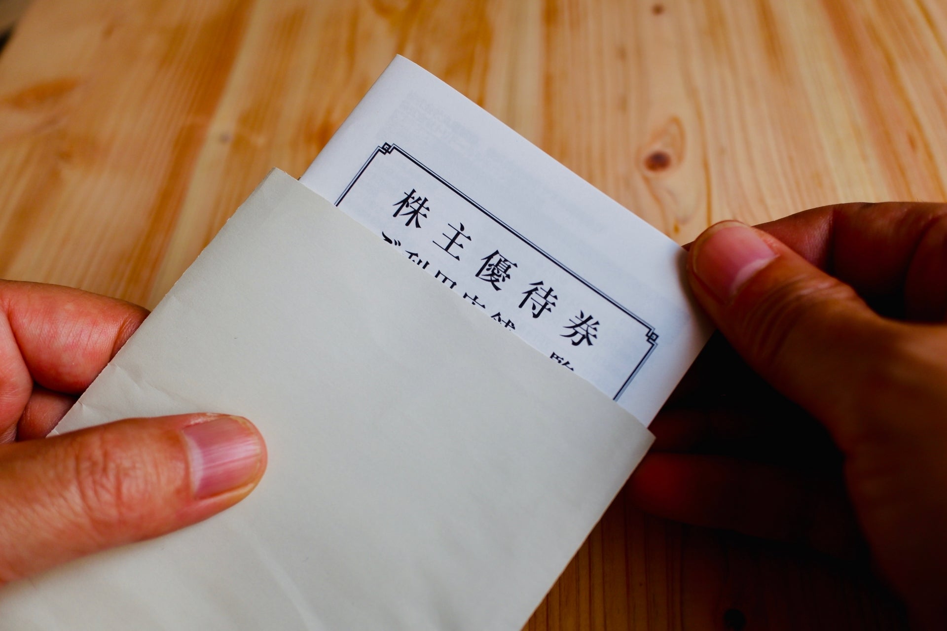 封筒から株主優待券が取り出されており、木目のテーブルの上で両手が書類を持っている