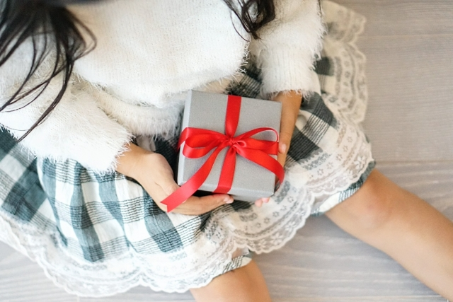 赤いリボンで包まれたグレーのギフトボックスを両手で持つ女性。給料日やボーナスの自分へのご褒美グルメを注文するシーン