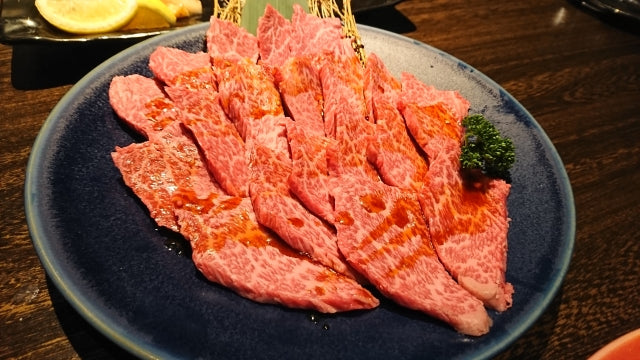 細かいサシが入った和牛のトモバラ系カルビが青い丸皿に並べられ、焼肉用に薄くスライスされた状態で提供されている