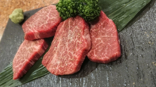 霜降りが美しい和牛ヒレ肉のスライスが石板の上に並び、わさびと葉物が添えられている