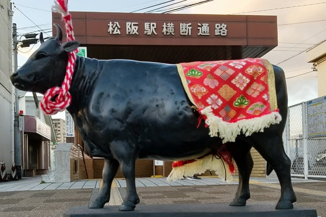 松阪駅横断通路前に展示された松阪牛の黒い牛の像に紅白の綱と赤い花柄の装飾布が掛けられている