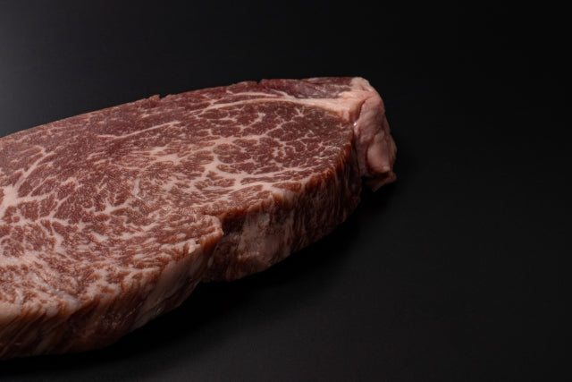 黒い背景に置かれた和牛のステーキ用厚切り肉。きめ細かな霜降りが全体に広がり、山形牛ならではの豊かなサシが際立つ断面