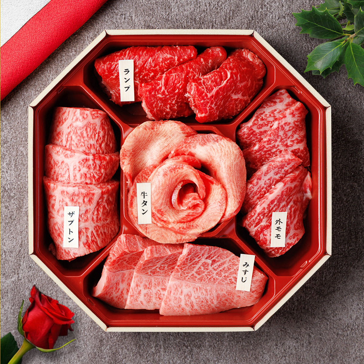 和牛セレブの食べ比べセット。八角形の折箱にランプ・牛タン・ザブトン・外モモ・みすじの5部位が部位札付きで盛り付けられ、中央に花タンのバラ、傍らに赤いバラが添えられている