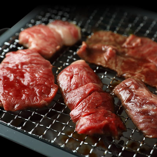 霜降りの神戸牛カルビが焼き網の上に乗り、表面がつやつやと輝きながら焼けていく焼肉の臨場感ある一コマ