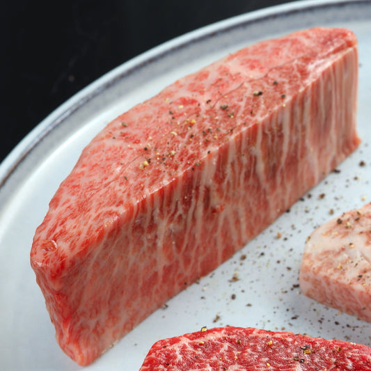 細かいサシが均一に入ったミスジのステーキ用ブロック肉が白いプレートの上に置かれ、粗挽き胡椒が散りばめられている