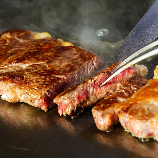 鉄板の上でサーロインステーキが焼き上げられ、トングで切り口を開くと中心部にほんのりピンクの火入れが確認できる