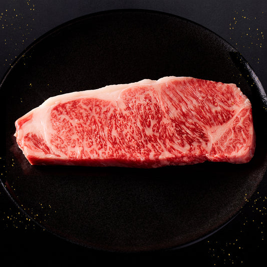 黒いプレートに置かれた能登牛サーロインステーキの断面で、赤身と白い霜降りが均一に広がっている
