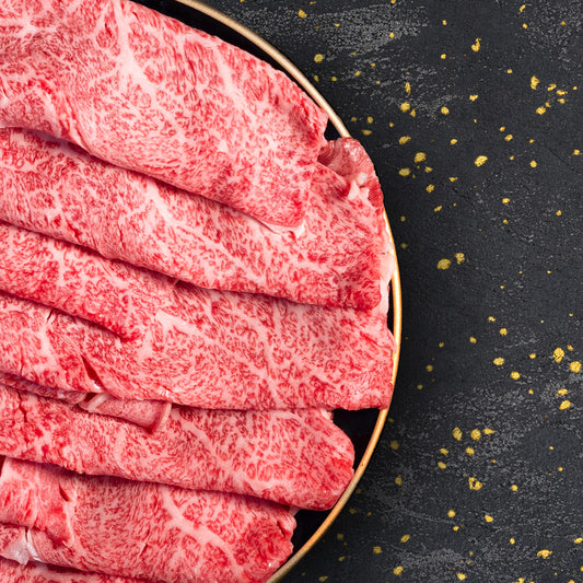きめ細かな霜降りが全面に広がる米沢牛ロースのスライス肉が、金縁の皿に丁寧に重ねて盛られている