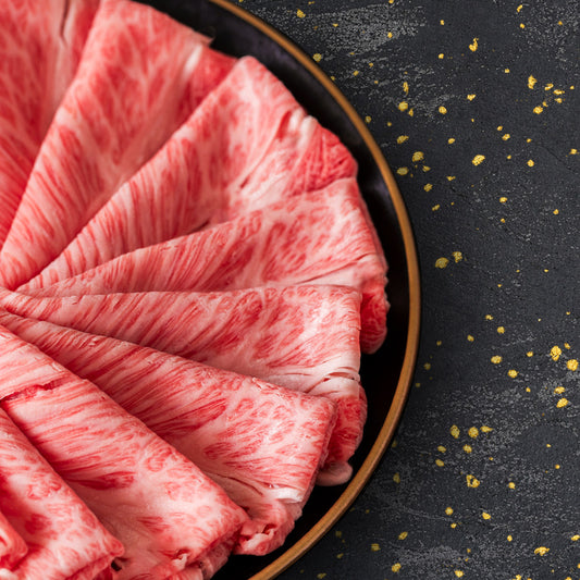 きめ細かな霜降りが均等に広がる薄切り牛肉が黒い丸皿の上に扇状に重なり、鮮やかなサシのパターンが際立つクローズアップ