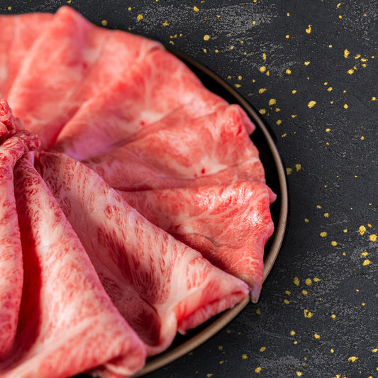 きめ細かな霜降りが美しい米沢牛リブロースの薄切り肉が、黒い皿の上に花びら状に重なり合って盛り付けられている