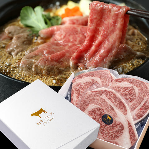 和牛セレブの黒毛和牛リブロースすき焼き。箸でつまみ上げた霜降り薄切り肉が鍋の上に広がり、白い化粧箱の前に整然と並んだ生のリブロース薄切り肉が添えられている