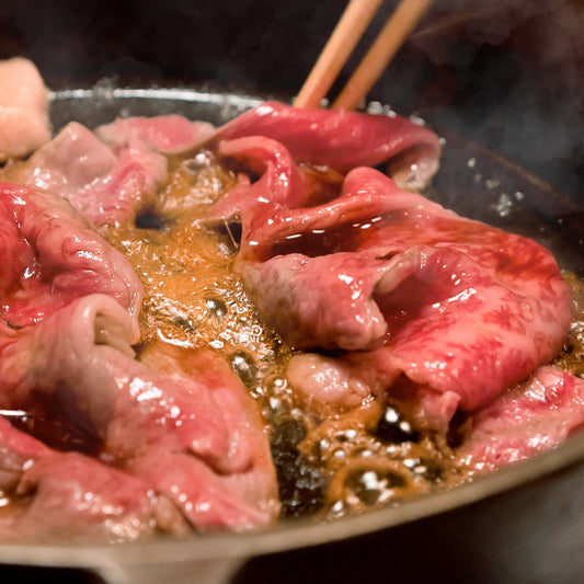 割り下で煮立つ鉄鍋の中で箸に持ち上げられた薄切り牛肉、湯気立ちのぼるすき焼きの臨場感ある調理シーン