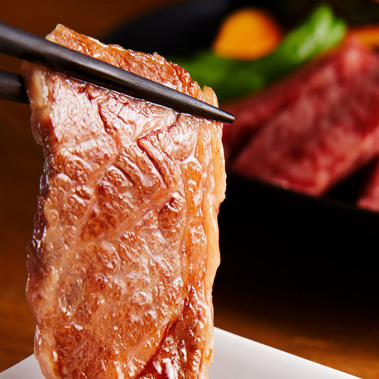 箸でつまみ上げた長崎和牛カルビのトモバラが焼き上がり、脂が滴るジューシーな断面と艶やかな照りが映し出されている